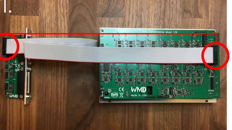A Performance Mixer (left) and DB25 expander (right) lying on a wooden surface, joined by a wide 20-pin ribbon cable. Red circles highlight the far-right 20-pin connector on the Performance Mixer and the 20-pin header at the top of the DB25 expander.